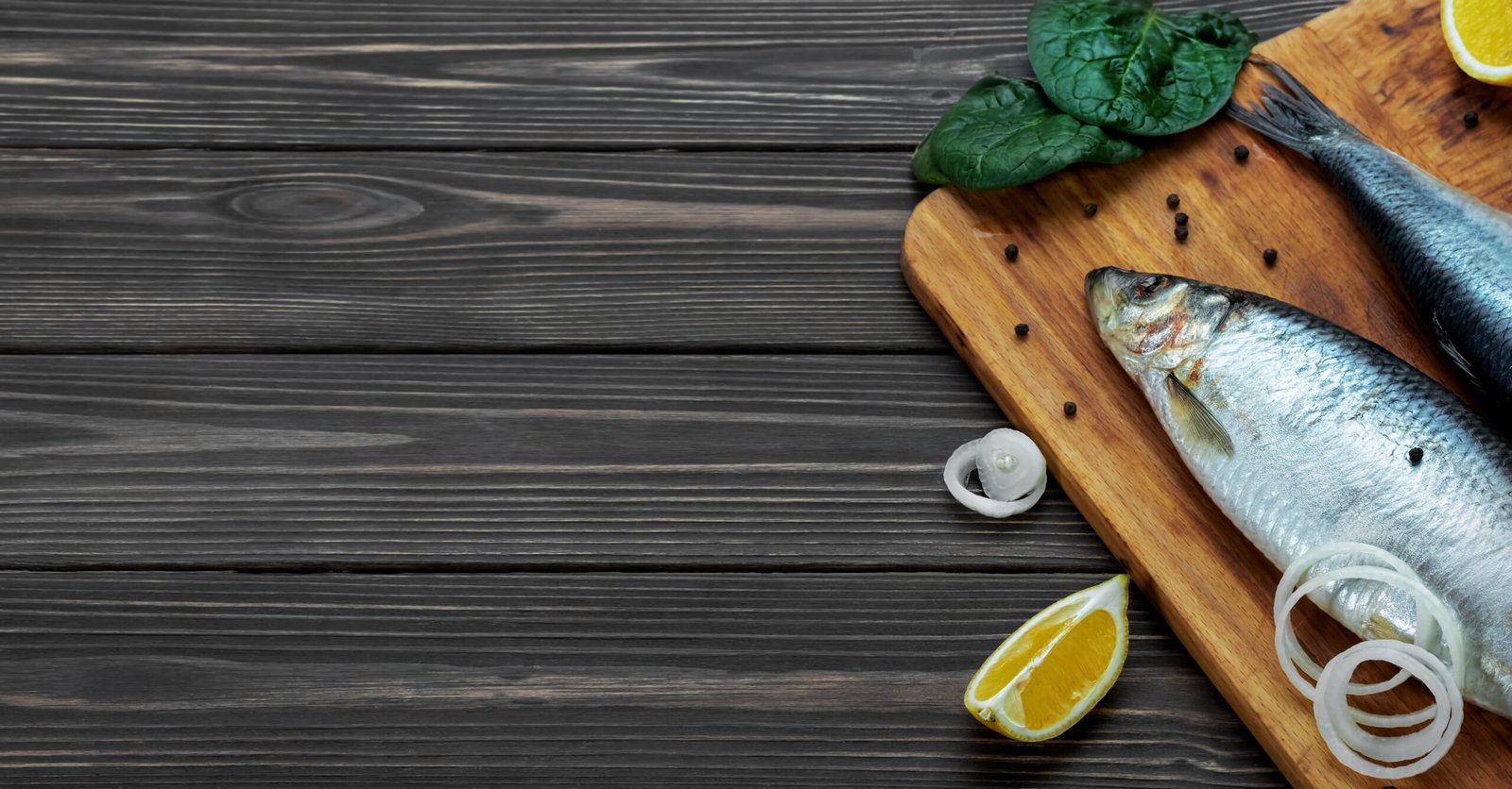 Making a Dutch Herring Sandwich – Haringhandel. Healthy seafood, pickled sea fish atlantic herring on a cutting board next to spices. Dark wooden background. Top view, copy space for text.